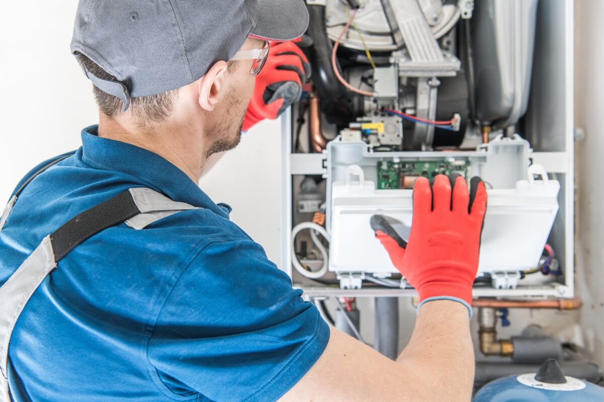 a person in a blue shirt and red gloves working on a gas furnace