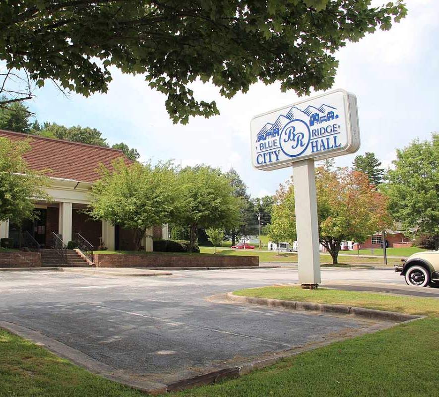 Exterior view of Blue Ridge City Hall, featuring a sign, trees, and a clean parking lot under a clear sky.