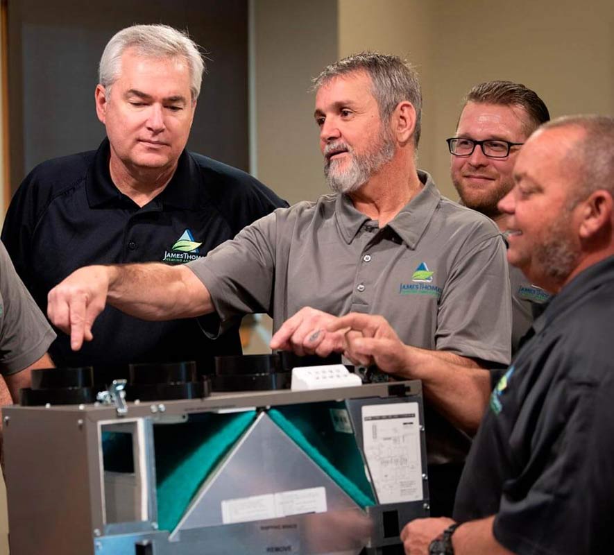 Five individuals in matching shirts are gathered around a mechanical unit, discussing its components and pointing at various parts.
