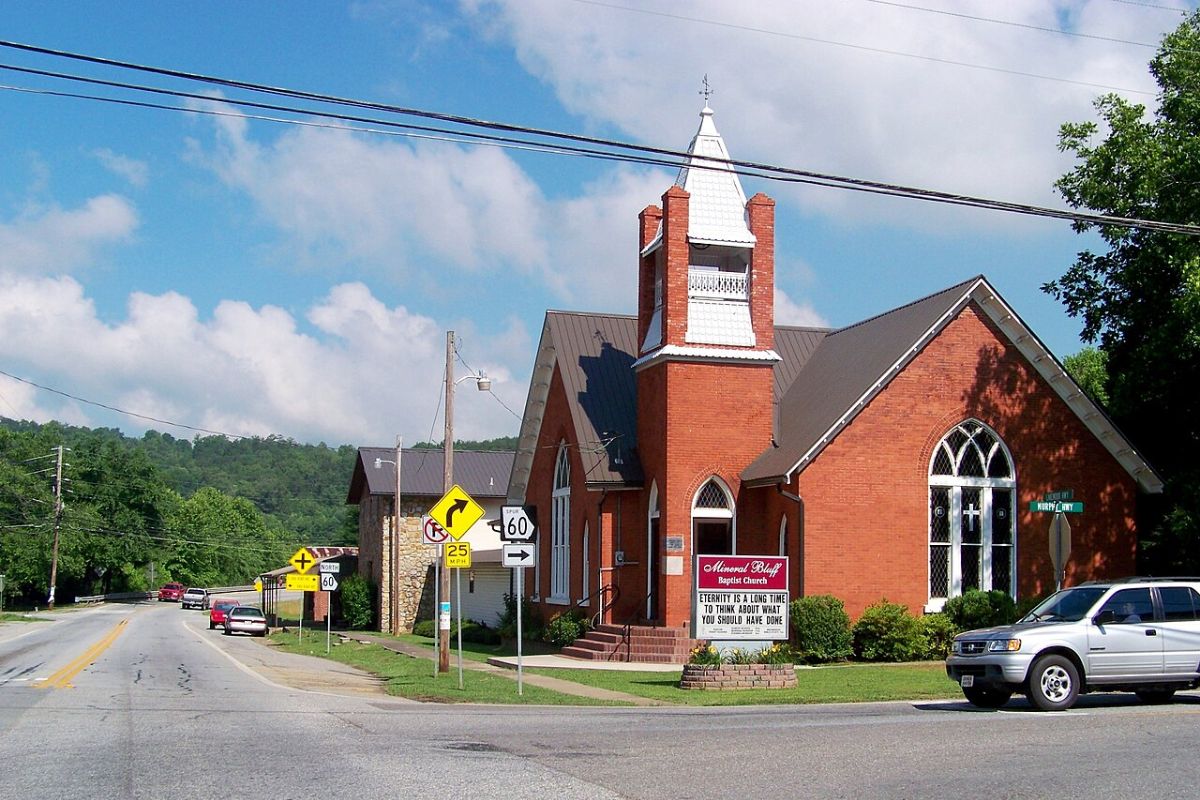 a church with a steeple and a sign on the side of the road