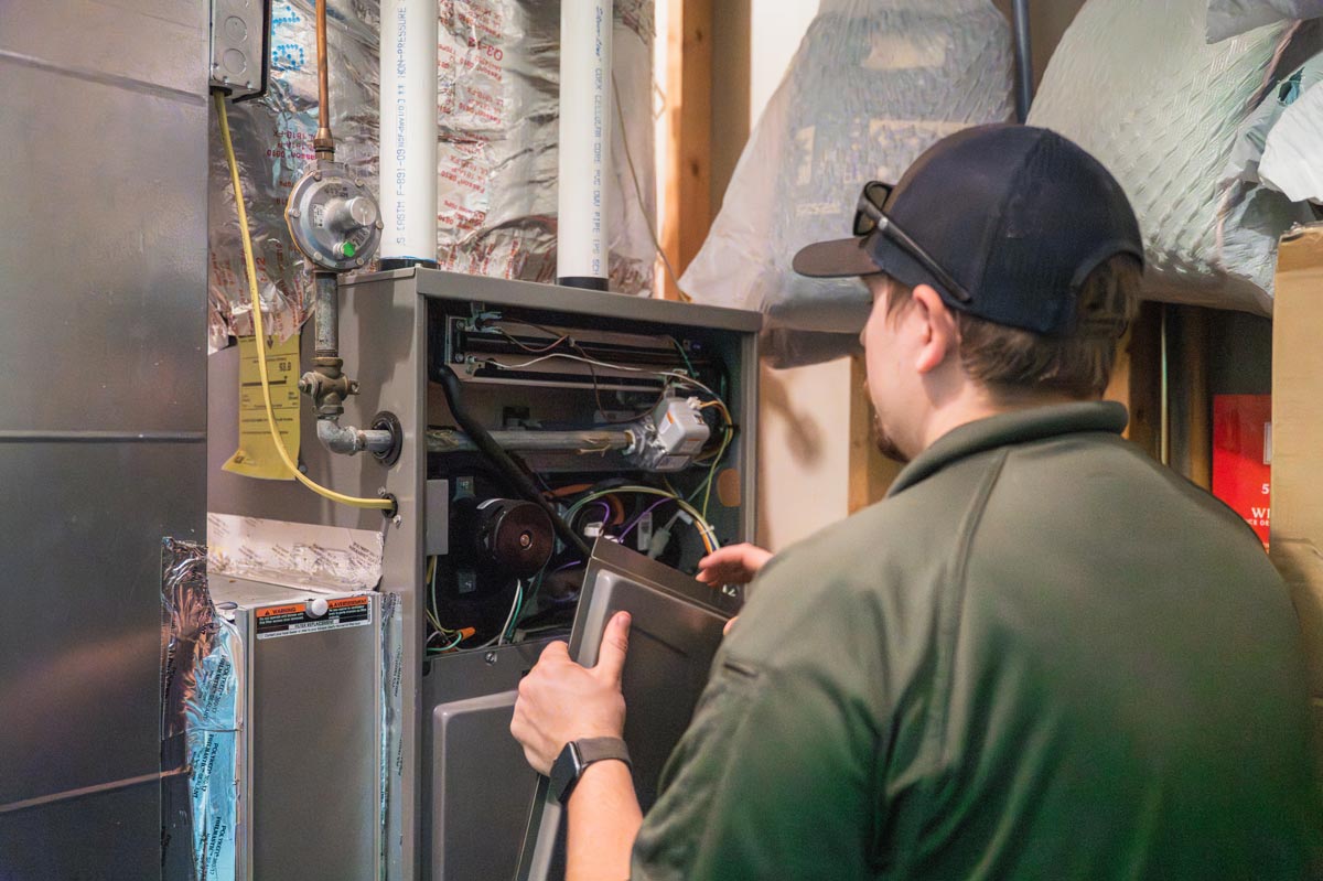 A technician of James Thomas Heating and Cooling is engaged in maintenance work on a furnace, surrounded by tools and equipment.