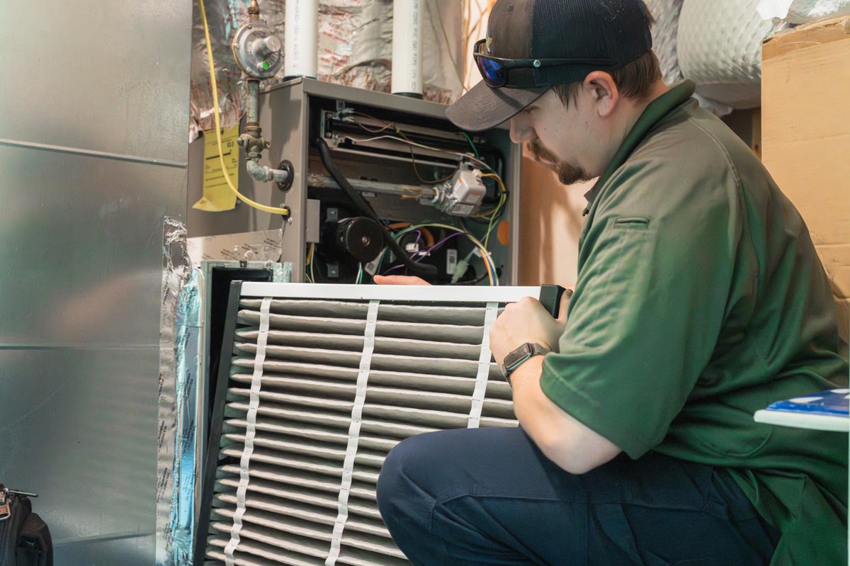 In a room, a man is servicing a furnace, paying close attention to the HVAC air filter for optimal performance.