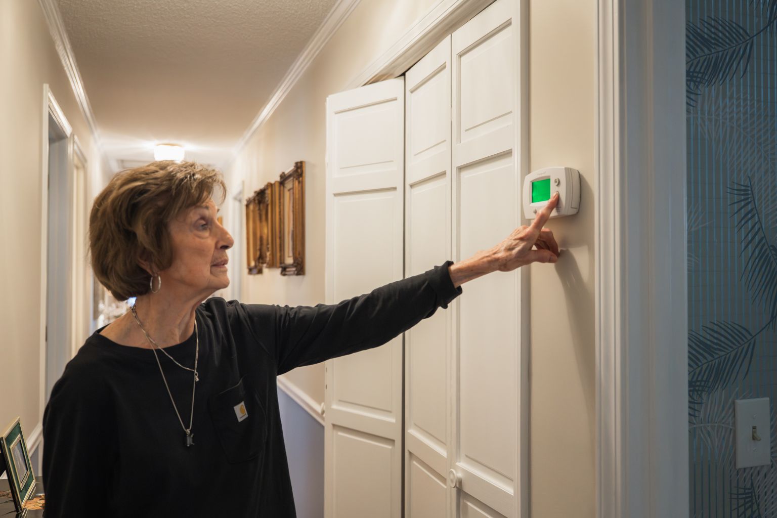 Homeowner adjusting wall thermostat in hallway to control indoor temperature and HVAC system