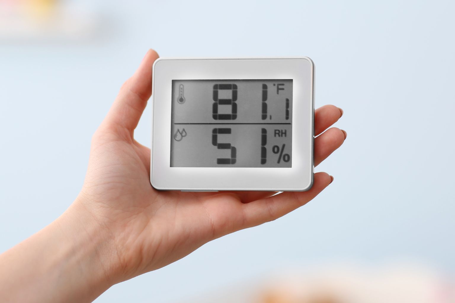 Hand holding a digital hygrometer displaying indoor temperature of 81.1°F and 51% relative humidity, illustrating accurate home humidity monitoring for comfort, health, and energy efficiency.