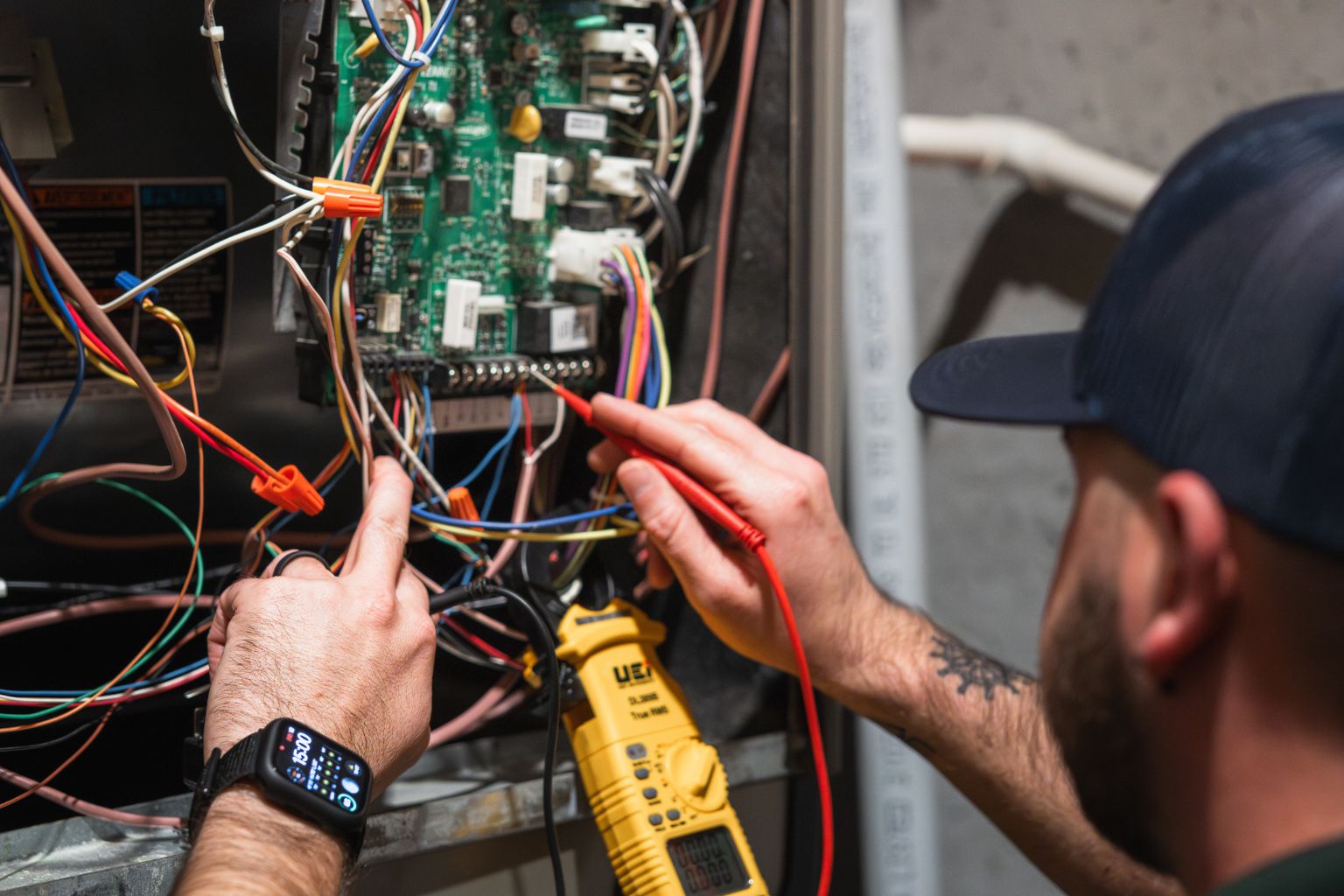 HVAC technician inspecting and testing an electrical control board with a multimeter, checking wiring and connections for proper functionality in a residential HVAC system, close-up view of hands, tools, and circuit components