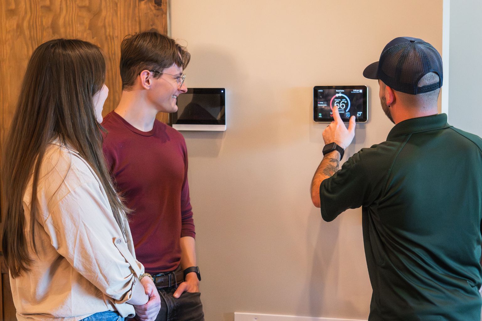 HVAC technician demonstrating smart thermostat operation to homeowners, optimizing indoor temperature and humidity control for energy efficiency and comfort.
